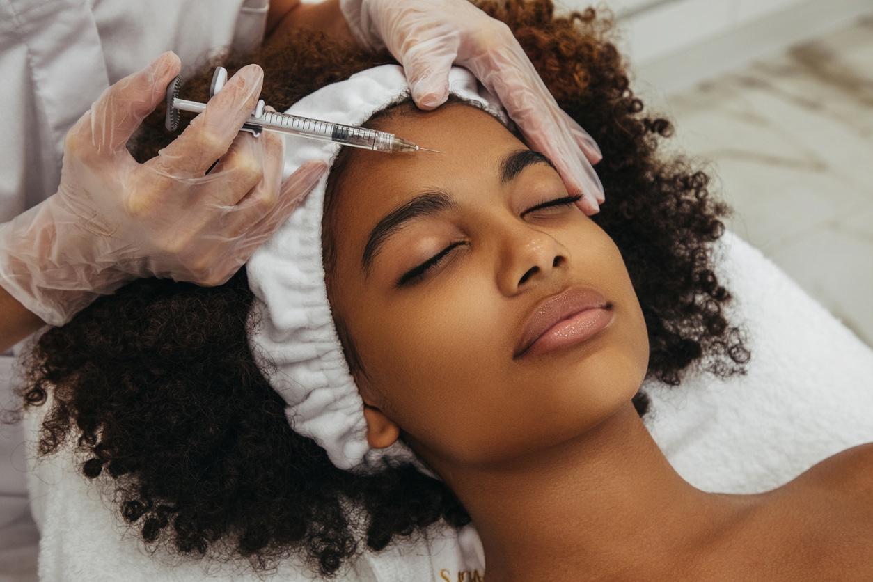 A provider administers a cosmetic facial injection to a patient’s forehead during an in-office treatment.